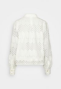 Blouse blanche à manches longues avec motifs en dentelle et œillets floraux, poignets boutonnés et col, vue de dos.