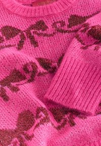 Rosa stickad tröja med fluffig textur som har ett brunt rosettmönster, rund halsringning och ribbade muddar.