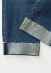 Donkerblauwe denim jeans met een raw hem en opgerolde lichtblauwe boorden. Onderscheidende stikdetails in een contrasterende gouden kleur.