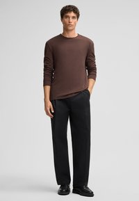 Braunes Langarmhemd aus weicher Baumwolle, kombiniert mit geraden schwarzen Hosen. Das Outfit hat einen klassischen Schnitt und ein minimalistisches Design.