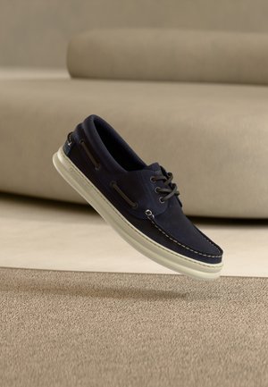 Marineblauer Bootsschuh aus Wildleder mit weißer Gummisohle. Verfügt über dekorative Nähte und eine Schnürung mit Metallakzenten.