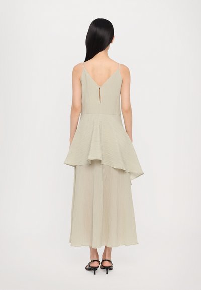 Light gray, textured dress with a peplum design, V-neck back, and asymmetrical hem. Thin straps and ankle-length, paired with black shoes.