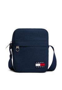 Borsa a tracolla blu navy realizzata in tessuto resistente. Presenta una chiusura con zip, tracolla regolabile e una toppa con il logo "TOMMY JEANS".