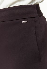 Černé šité kalhoty z texturované tkaniny, s elegantním kovovým akcentem a klasickým designem s čistými liniemi a bočními kapsami.