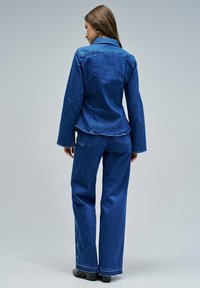 Veste en denim à manches longues et col, associée à un pantalon en denim à jambes larges. Les deux sont de bleu moyen, présentant une finition lisse et texturée.