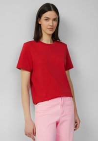 Rode katoenen T-shirt met korte mouwen en een ronde hals, gecombineerd met lichtroze jeans. Zachte textuur, casual pasvorm.