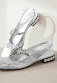 Hopeasaumaiset slingback-laput, joissa on pyöreä kärki, koristeellinen strassihihna ja pieni tukikorko. Sujuva pinta.