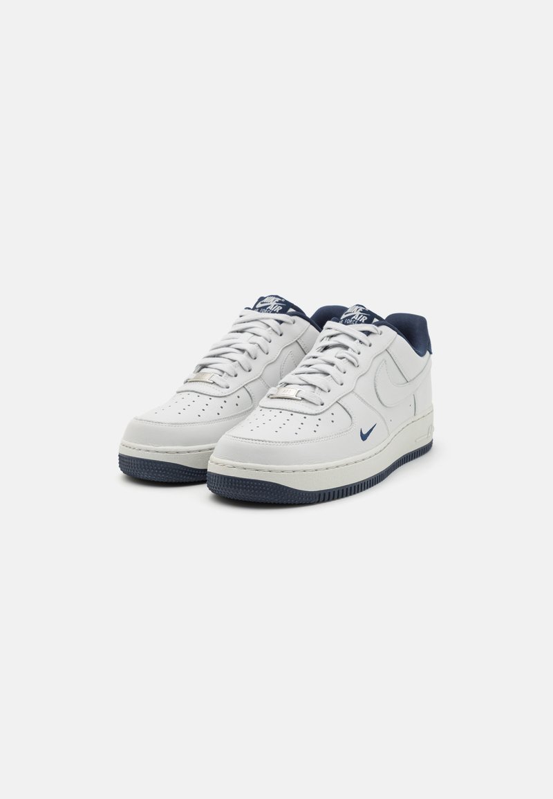 Białe skórzane sneakersy z granatowymi akcentami, perforowanym przodem, zaokrąglonym kształtem i teksturowaną ciemną podeszwą. Posiadają sznurowadła i logo na języku.