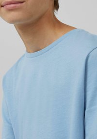 Lichtblauw katoenen t-shirt met een klassieke ronde hals. Zachte textuur en korte mouwen, met een ontspannen pasvorm en minimale stikseldetails.