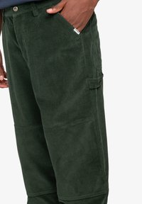 Groene corduroy broek met een gestructureerd oppervlak, zijzak en verstevigde knie naden. De stof heeft een zachte, ribbelige uitstraling.