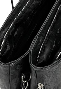 Interno di una borsa in pelle nera testurizzata con due scomparti con zip foderati in un tessuto nero a motivi. Accenti in metallo visibili.