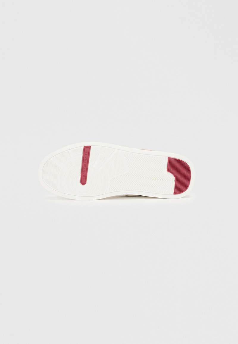 Semelle de sneaker blanche avec accent rouge, en caoutchouc texturé pour l'adhérence, dotée d'un motif de marche géométrique et d'une bande contrastante sur le talon.