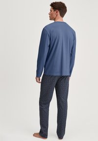 Lange mouwen blauwe shirt met een ronde hals, gecombineerd met gestreepte marineblauwe broek met een spiraalontwerp in rood en wit. Relaxte pasvorm en een gladde textuur.