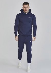 Felpa con cappuccio blu navy e pantaloni della tuta abbinati, realizzati in materiale morbido, con una tasca frontale e un logo sul petto e sulla coscia.