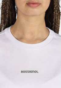 Camiseta de algodón blanca con cuello redondo y mangas cortas, que presenta un logo gris "ROSSIGNOL" centrado en el pecho.