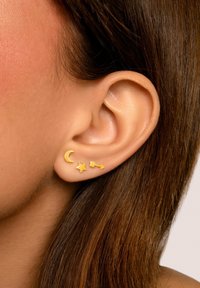 Goldene Steckerohrringe mit Designs von einer Halbmond, einem Stern und einem Pfeil. Glatte, glänzende Oberflächen mit einer minimalistischen Ästhetik.