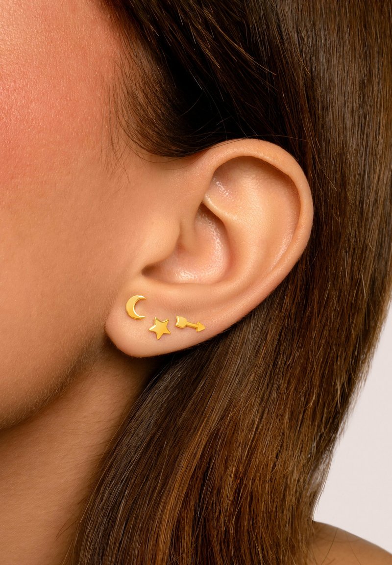 Goldene Steckerohrringe mit Designs von einer Halbmond, einem Stern und einem Pfeil. Glatte, glänzende Oberflächen mit einer minimalistischen Ästhetik.