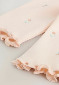 Jasnoróżowa dzianina z falbaniastymi mankietami, zdobiona drobnym haftem w pastelowych kolorach. Miękka tekstura i dopasowany krój.