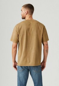 Braunes, kurzärmliges T-Shirt aus weichem Stoff. Hat eine lockere Passform und saubere Nähte. Wird mit blauen Jeans getragen.