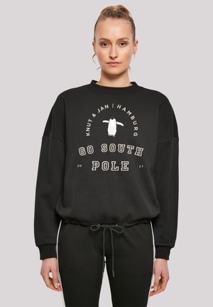 Schwarz sweatshirt mit einem lockeren Schnitt, das ein Pinguin-Graphic und den Text "GO SOUTH POLE" in Beige zeigt. Elastischer Saum und Bündchen.