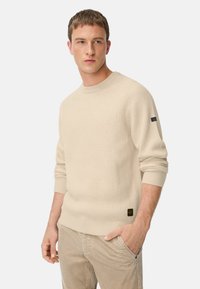Beige gerippter Strickpullover mit einem Rundhalsausschnitt, langen Ärmeln und schwarzen Akzenten an den Ärmeln und am Saum. Weicher Stoff, leicht taillierte Form.