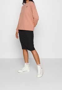 Felpa rosa con un piccolo logo giallo, abbinata a una gonna nera a lunghezza ginocchio e sneakers bianche alte. Tessuto morbido, vestibilità casual.