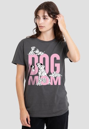 Woman wearing a dark gray t-shirt with pink "DOG MOM" text and cartoon Dalmatian dogs around the letters on a plain background.