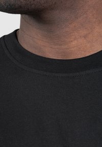 Musta crewneck-t-paita, jossa on sileä, teksturoitu kangas, tiukasti istuva kaulus ja siisti ommel kaula-aukon ympärillä.