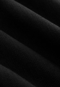Gros plan d'un tissu noir plié montrant une texture fine en tricot et des ombres douces à la surface.