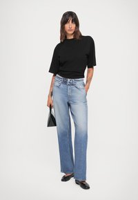 Svart t-skjorte med korte ermer, lyseblå vide jeans, glatt tekstur, ankellang, kombinert med svarte leiligheter og en liten svart veske.
