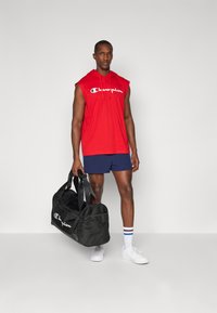 Red sleeveless hoodie with white "Champion" logo, navy shorts, black duffel bag, white sneakers, colored striped socks. Simple design elements.