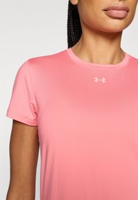 Ροζ αθλητική μπλούζα με κοντά μανίκια και στρογγυλή λαιμόκοψη, κατασκευασμένη από λείο ύφασμα. Διαθέτει μικρό  λευκό λογότυπο της Under Armour στο στήθος.