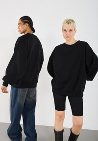 Felpe nere oversize con maniche scese, abbinate a jeans scuri e pantaloni sportivi neri. Tessuto morbido e vestibilità rilassata.