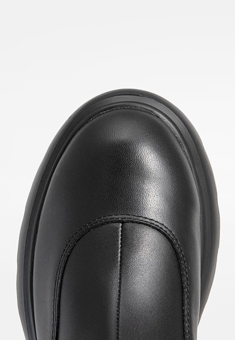 Schwarzer Leder-Ankle-Boot mit runder Zehenpartie, glatter Textur und subtilen Nahtdetails. Gummisohle mit leichtem Rand rund um die Kante.