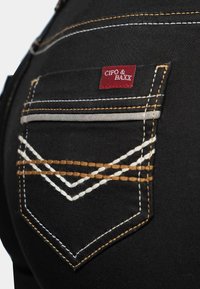 Zwarte denim spijkerbroek met een achterzak met decoratieve stiksels in wit en bruin, en een rood label met de tekst "CIPO & BAXX."
