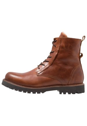 Brauner Leder-Schnür-Stiefelette mit schwarzer robuster Sohle und Zuglaschen an Ferse und hinten, im Seitenprofil vor weißem Hintergrund gezeigt.