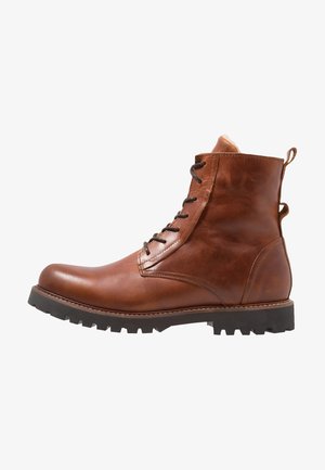 Bota de cuero marrón con cordones, suela negra resistente y lengüetas para tirar en el talón y atrás, mostrada de perfil sobre fondo blanco.