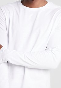 Langärmliges weißes T-Shirt aus weichem Stoff, mit Rundhalsausschnitt und schmalen Ärmel, mit glatter Textur und ohne sichtbare Muster.