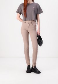 Camiseta gris recortada con gráfico, jeans ajustados beige, zapatos negros de plataforma sin cordones y un bolso negro. Tejido suave y ajuste entallado.