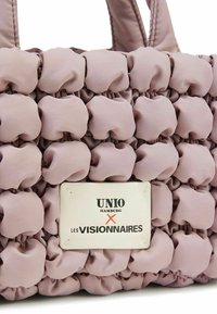 Sac à main matelassé rose avec un design en forme de losanges, présentant une étiquette blanche sur laquelle est écrit "UNIO HAMBURG X LES VISIONNAIRES." Texture lisse et poignées robustes.
