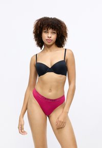 Czarny biustonosz wypełniony z regulowanymi ramiączkami, w połączeniu z różowymi majtkami w stylu bikini z czarnym pasem Calvin Klein. Gładka faktura materiału.