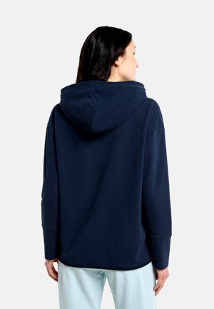 Marineblauer Hoodie mit großzügiger Kapuze, lässiger Passform, langen Ärmeln und weichem Baumwollmaterial, getragen zu hellblauen Hosen.