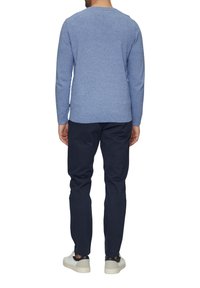 Niebieski sweter dzianinowy z długimi rękawami, okrągłym dekoltem i fakturowaną tkaniną. Połączony z ciemnoniebieskimi spodniami i białymi trampkami, widziany od tyłu.