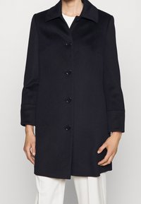 Black wool coat with a relaxed fit, featuring a notched collar, five button closures, and long sleeves. Smooth texture and clean lines.