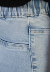 Gros plan sur un tissu en denim bleu clair montrant descoutures détaillées et la couture de poche sur un pantalon ou une jupe.