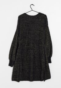 Černý dlouhý rukáv pletený svetr se zlatými kovovými nitěmi, zavěšený na černém ramínku na bílém pozadí.