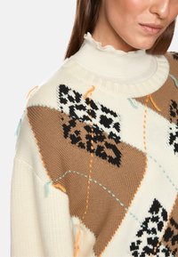 Knit sweater featuring leopard and diamond patterns in beige, cream, and black, with decorative stitching in orange and blue accents.