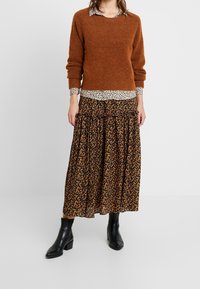 Brązowy, puszysty sweter nałożony na biało-czarny kołnierz w wzór panterki, połączony z czarną, kwiecistą spódnicą maxi i czarnymi botkami za kostkę.