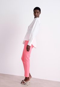 White long-sleeve blouse with puffed shoulders paired with fitted pink trousers and heeled sandals, showcasing a smooth texture and modern silhouette.
