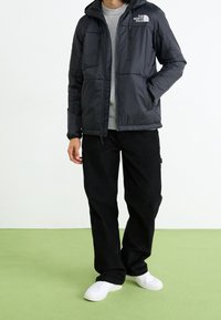 Černá péřová bunda s kapucí, se zapínáním na zip, dvěma zipovými kapsami a logem na hrudi, v kombinaci s černými manšestrovými kalhotami a bílými teniskami.